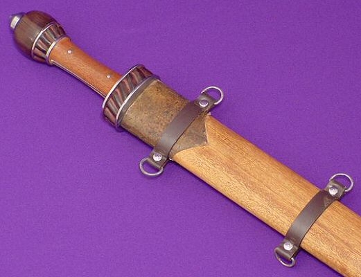 Close up of the SR061 Roman Spatha hilt. In this angle, you can just barely see the full tang visible on either side of the handle. The guard has two wood sections with a spiral texture, capped with brass plates. The steel pommel helps with balance.